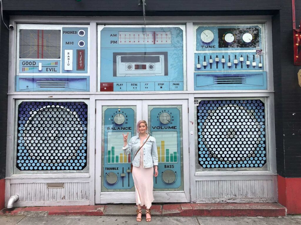 Woman stands in front of shop windows painted to look like a big boombox