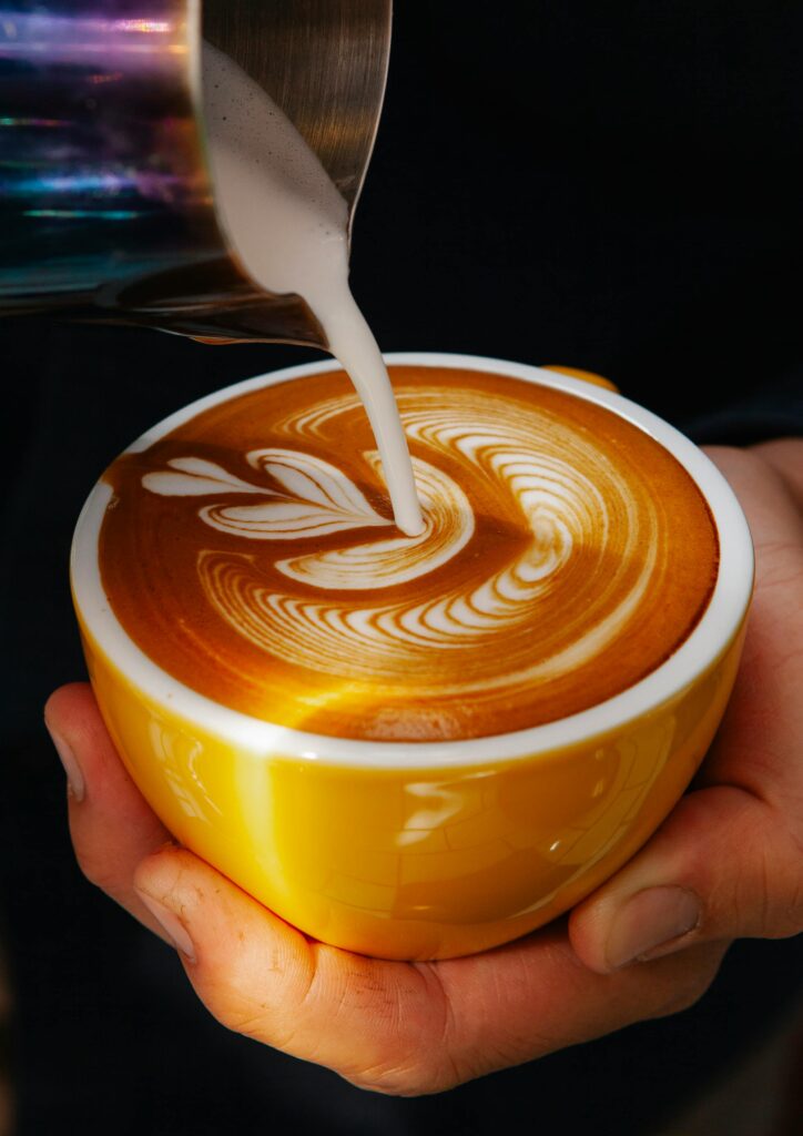 A hand is pouring steamed milk into an espresso drink creating beautiful latte art