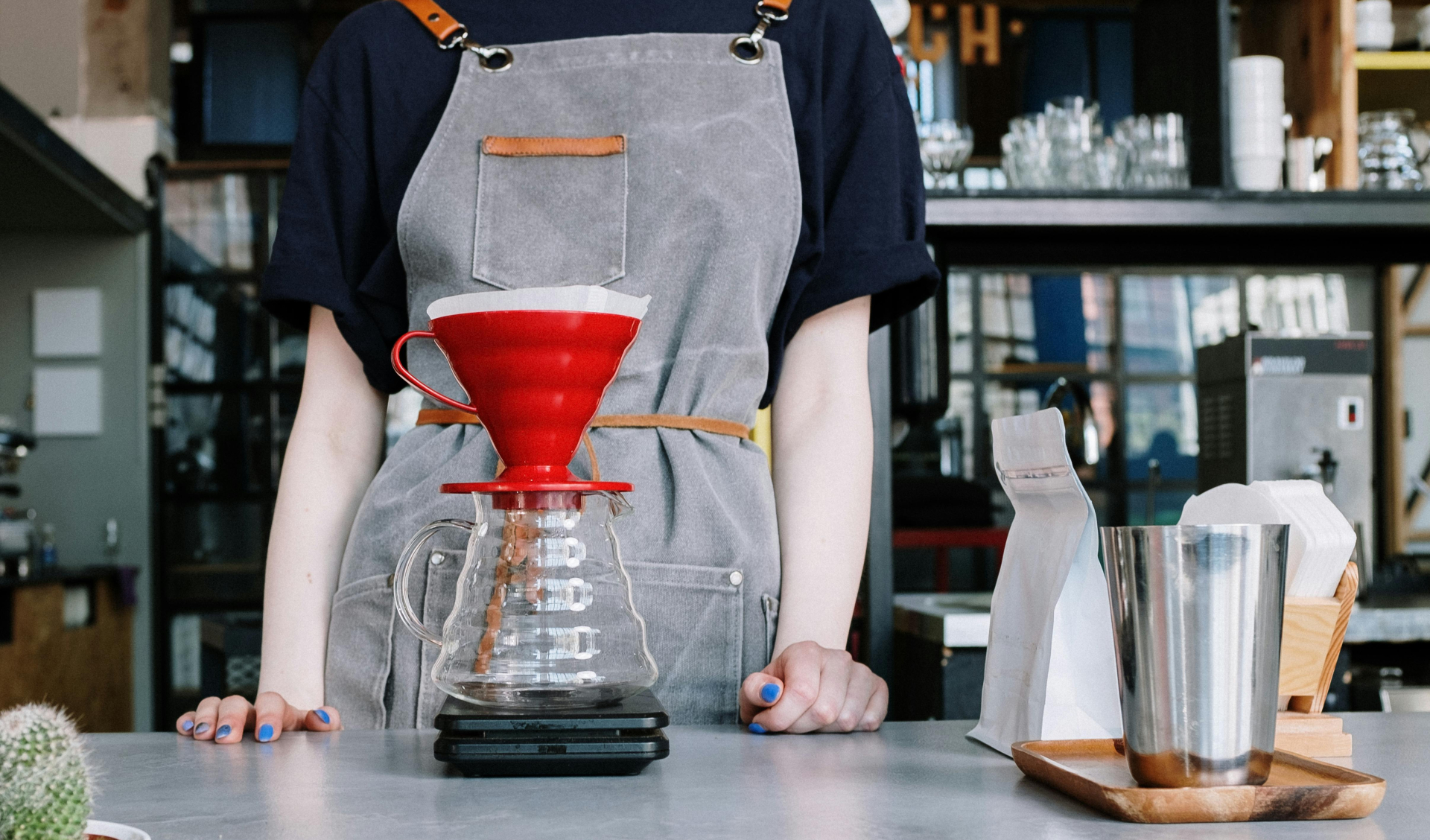 A barista is making a pour-over coffee with a glass coffee pot and a red filter