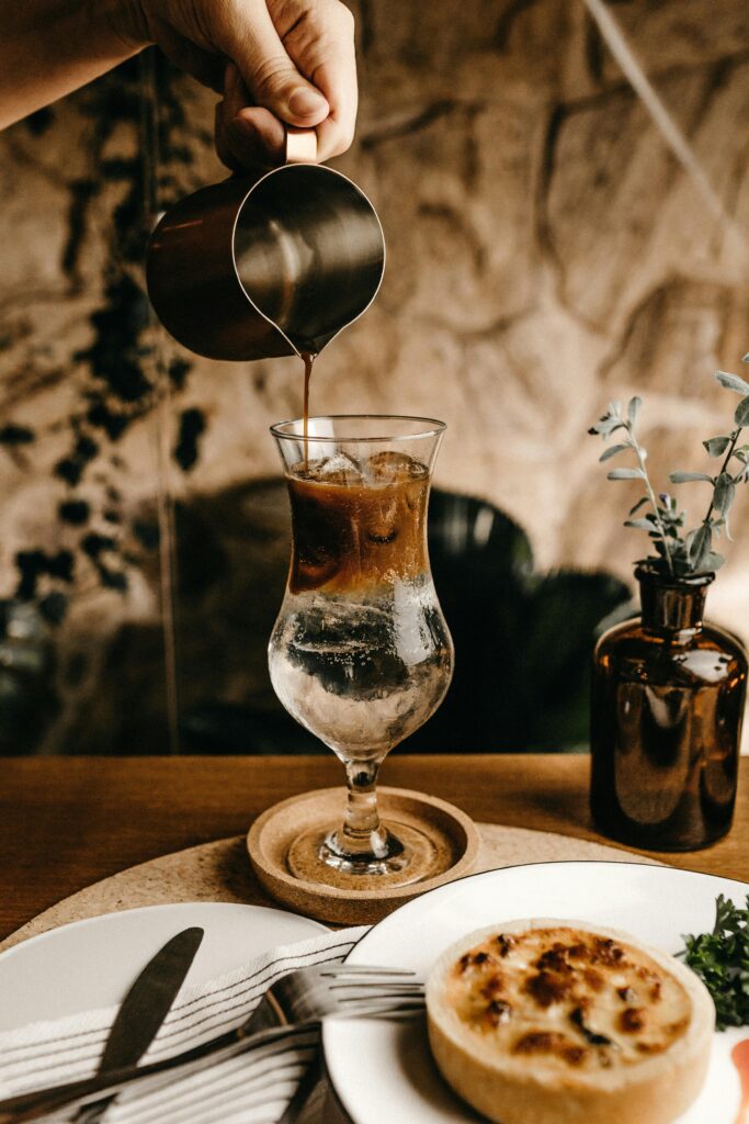 A hand is pouring espresso into a glass full of tonic water with a stone background