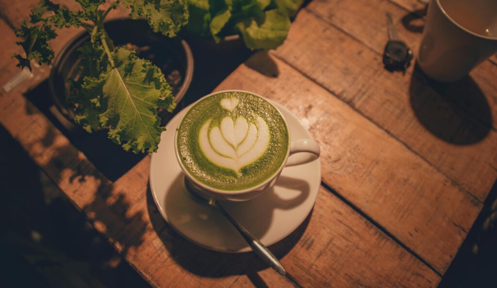 A green matcha latte with beautiful latte art hearts on top resting on a wood table